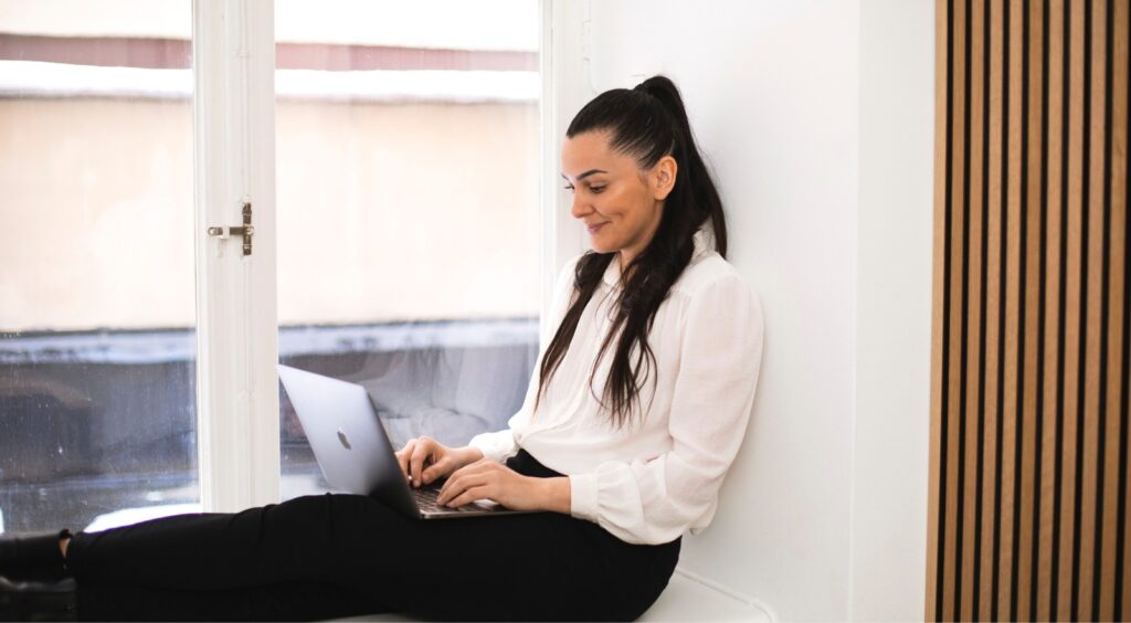 Kvinna som sitter i ett fönster med en dator i knät.